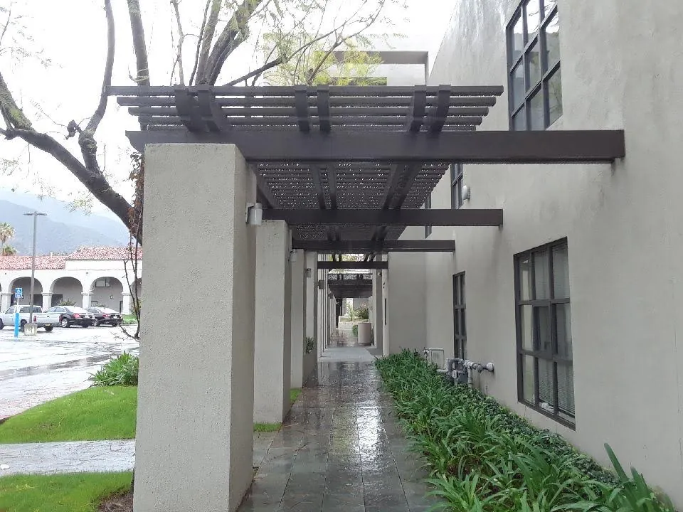 Dark-finish pergola over a landscaped building entry walkway